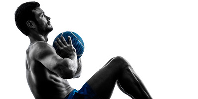 Effektives Bauchtraining: Foto von einem Mann beim Training der Bauchmuskeln mit einem Medizin-Ball mit freiem Oberkörper.